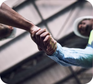 Two Construction Workers Hard Hats Shake Hands Warehouse Two construction workers in hard hats shake hands in a warehouse.