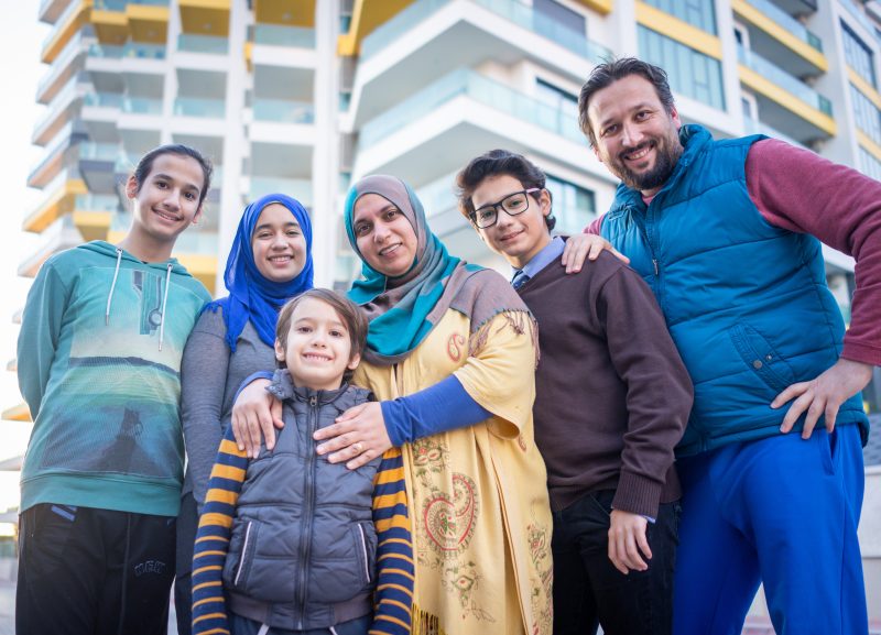 Smiling Family Six Including Parents Four Children Poses A smiling family of six, including parents and four children, poses for a photo in front of a modern apartment building.