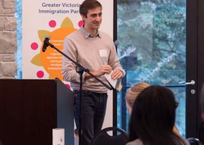 A white man in a light-coloured sweater and jeans walks away from a podium with a microphone.