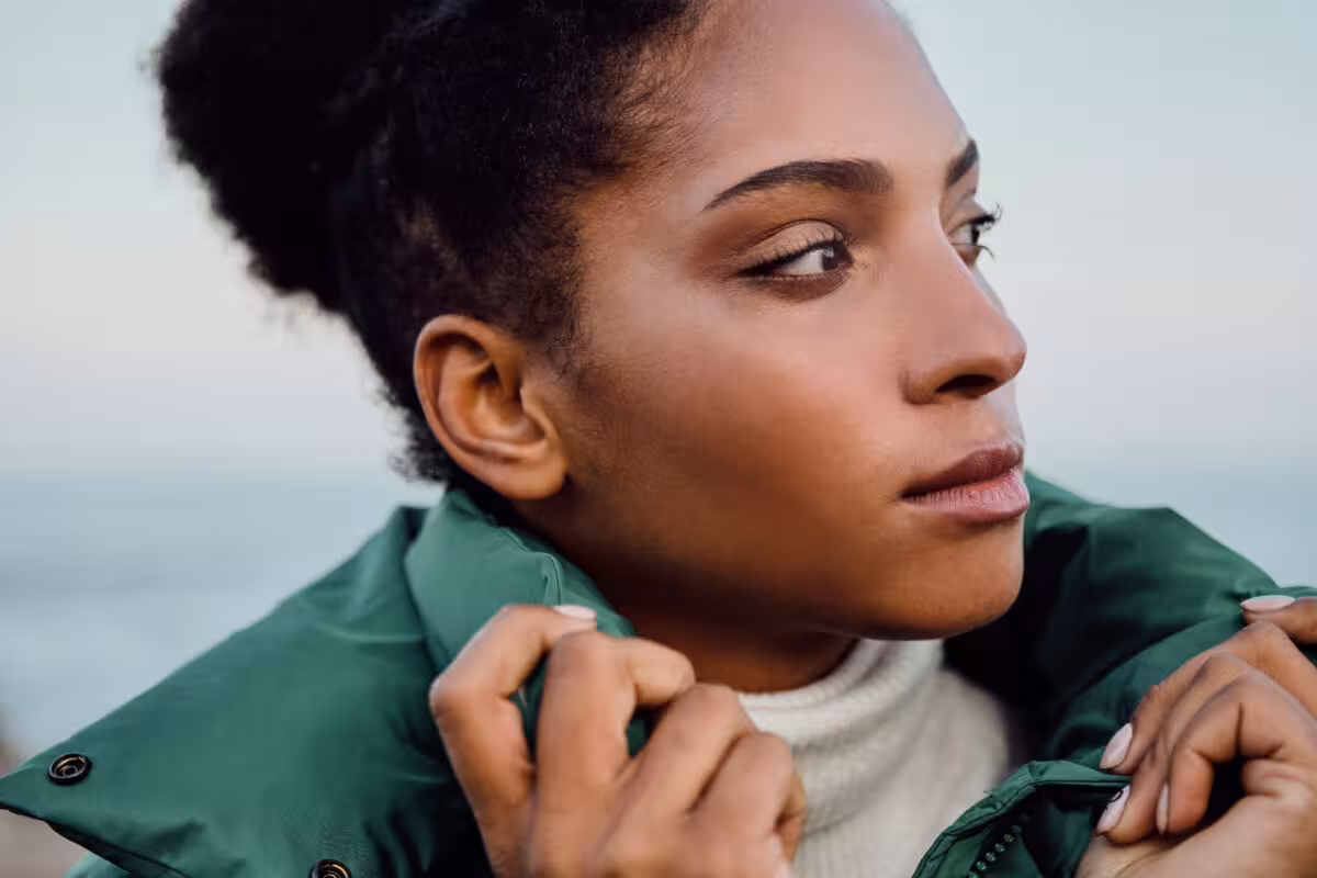 Closeup Profile Black Woman Wearing Green Puffer Jacket Close-up profile of a Black woman wearing a green puffer jacket and white turtleneck, looking to the right.
