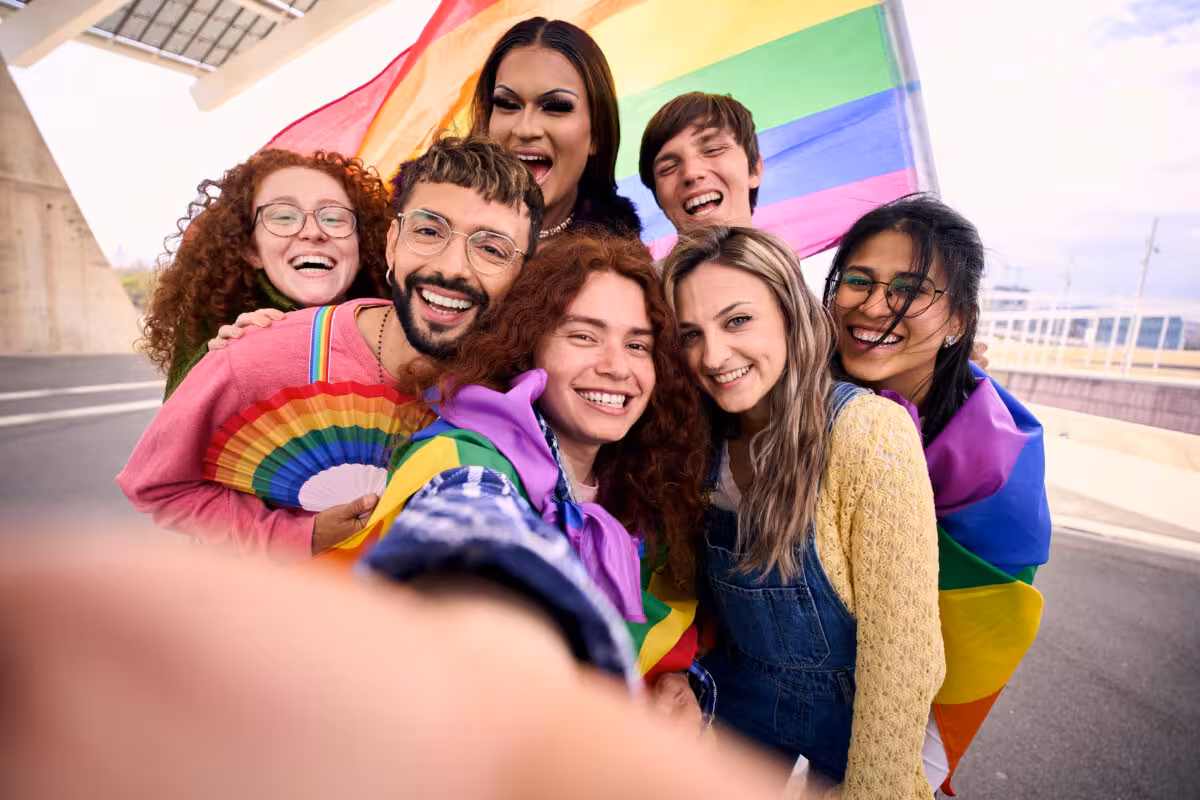 Diverse Group Seven Smiling People Pose Selfie Rainbow A diverse group of seven smiling people pose for a selfie with a rainbow flag and fan, celebrating Pride.