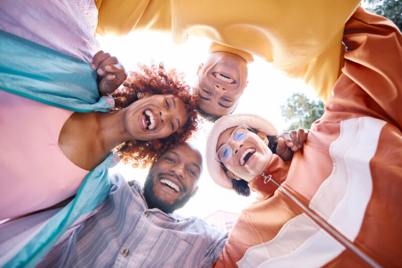 Four Friends Laugh Together Circle From Low Angle Four friends laugh together in a circle from a low angle, looking up at the camera.