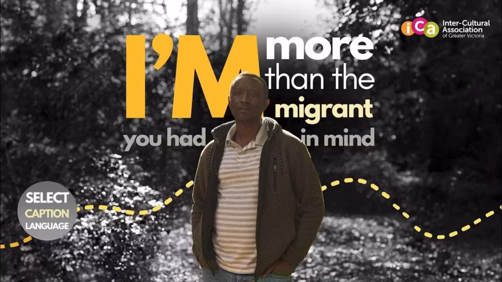 A black man with a striped collared shirt and olive jacket standing in front of text that says "I'm more than the immigrant you had in mind.
