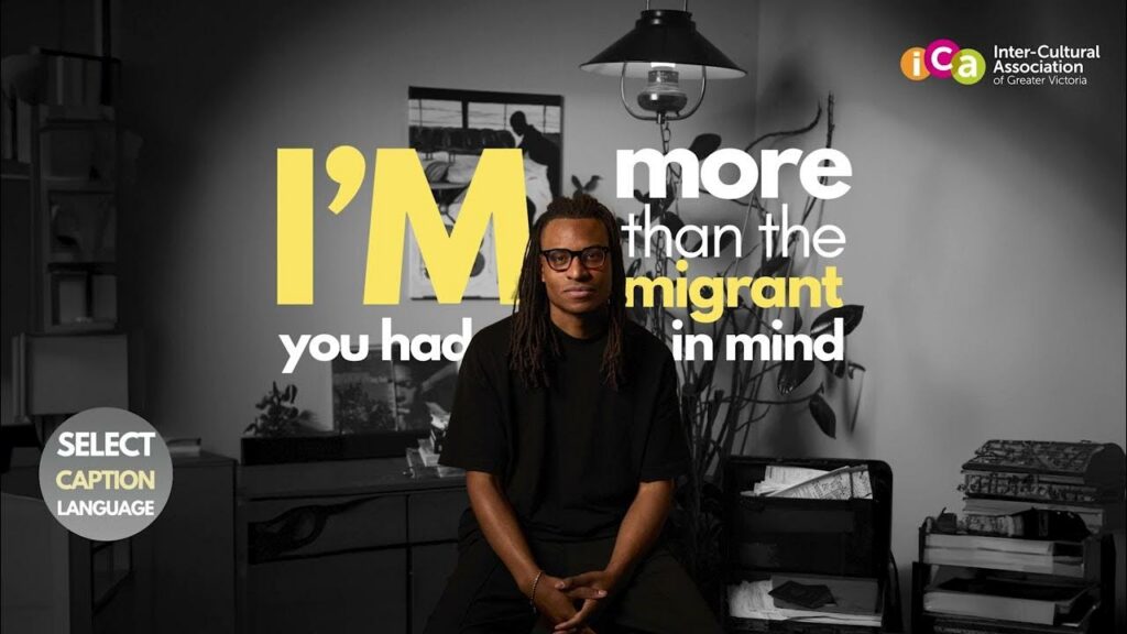 A man with dreadlocks and glasses sits looking forward, with text on screen reading "I'M more than the immigrant you had in mind.