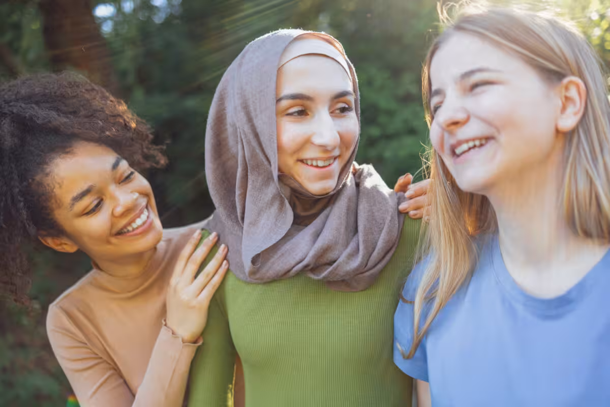 Three Young Women Diverse Backgrounds Smiling Laughing Outdoors Three young women of diverse backgrounds smiling and laughing outdoors in dappled sunlight.