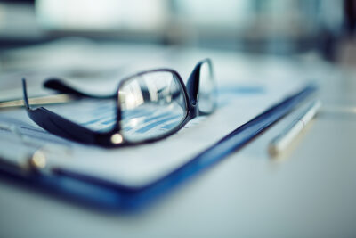 Black-rimmed glasses and a pen rest on business graphs on a clipboard.
