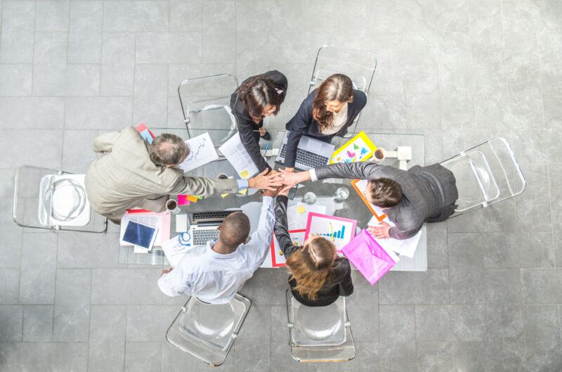 A diverse group of business professionals put their hands together in a sign of unity and teamwork.