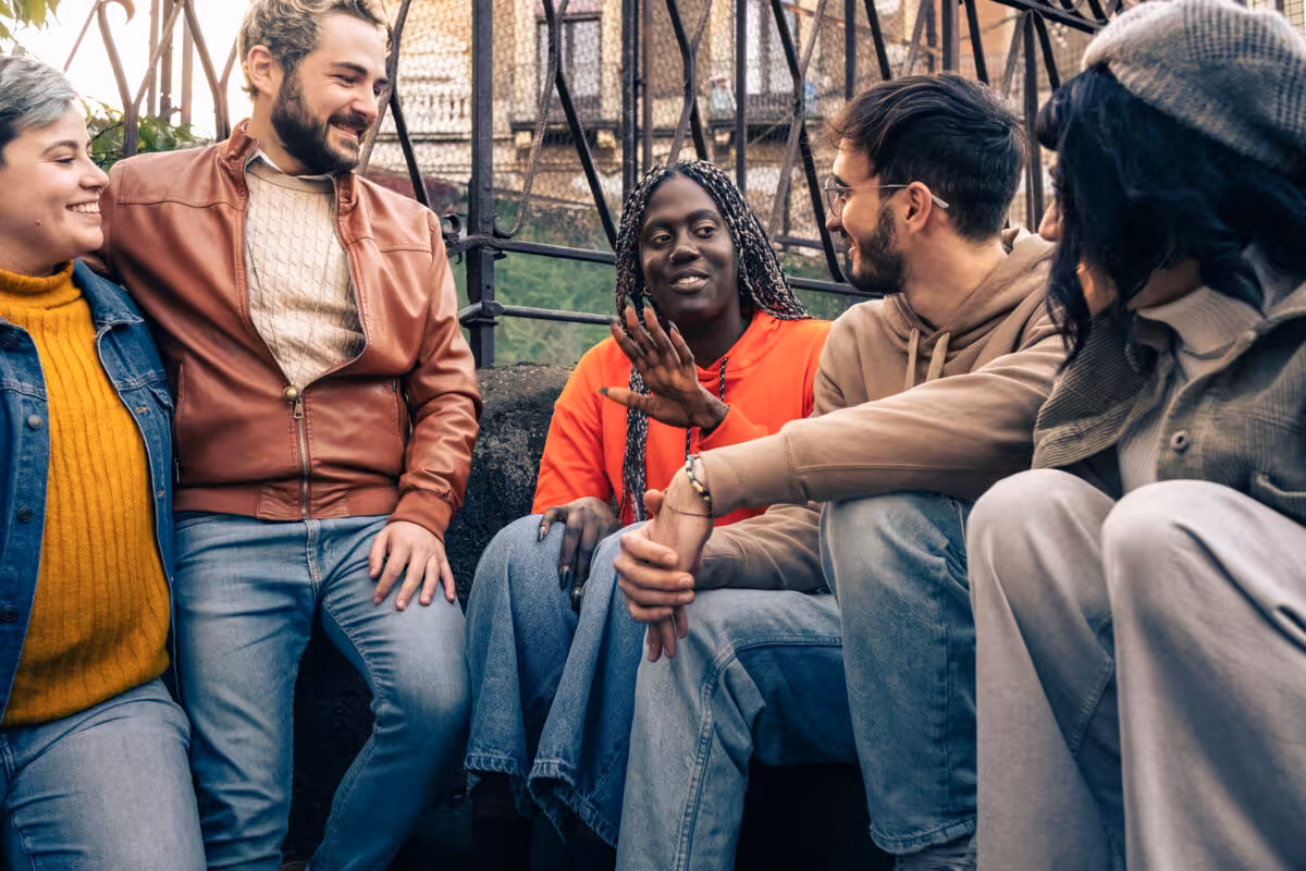 Diverse Group Five Young Adults Sit Together Smiling A diverse group of five young adults sit together, smiling and talking outdoors.