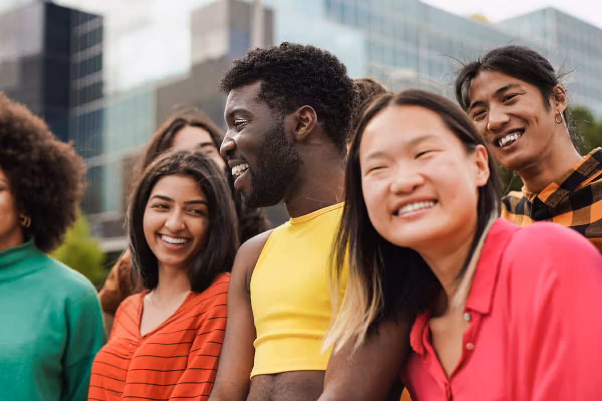 A diverse group of young people are smiling and laughing together outdoors.