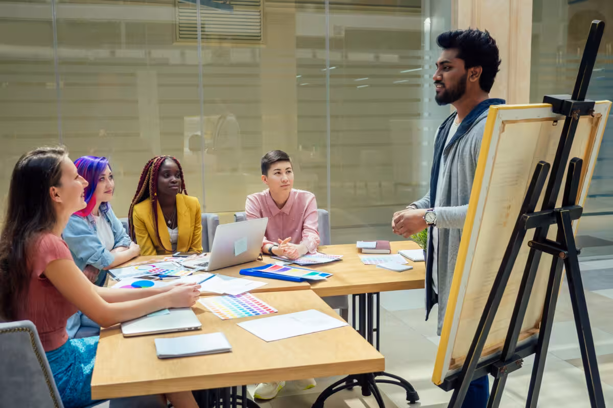 Man Presents Diverse Group People Sitting Tables Modern A man presents to a diverse group of people sitting at tables in a modern meeting room.