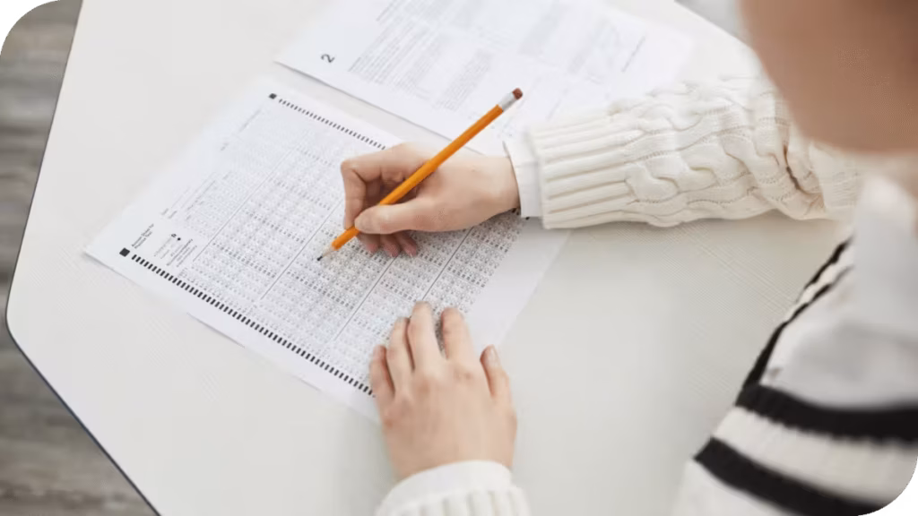A person's hands are shown filling out a bubble sheet with a pencil.