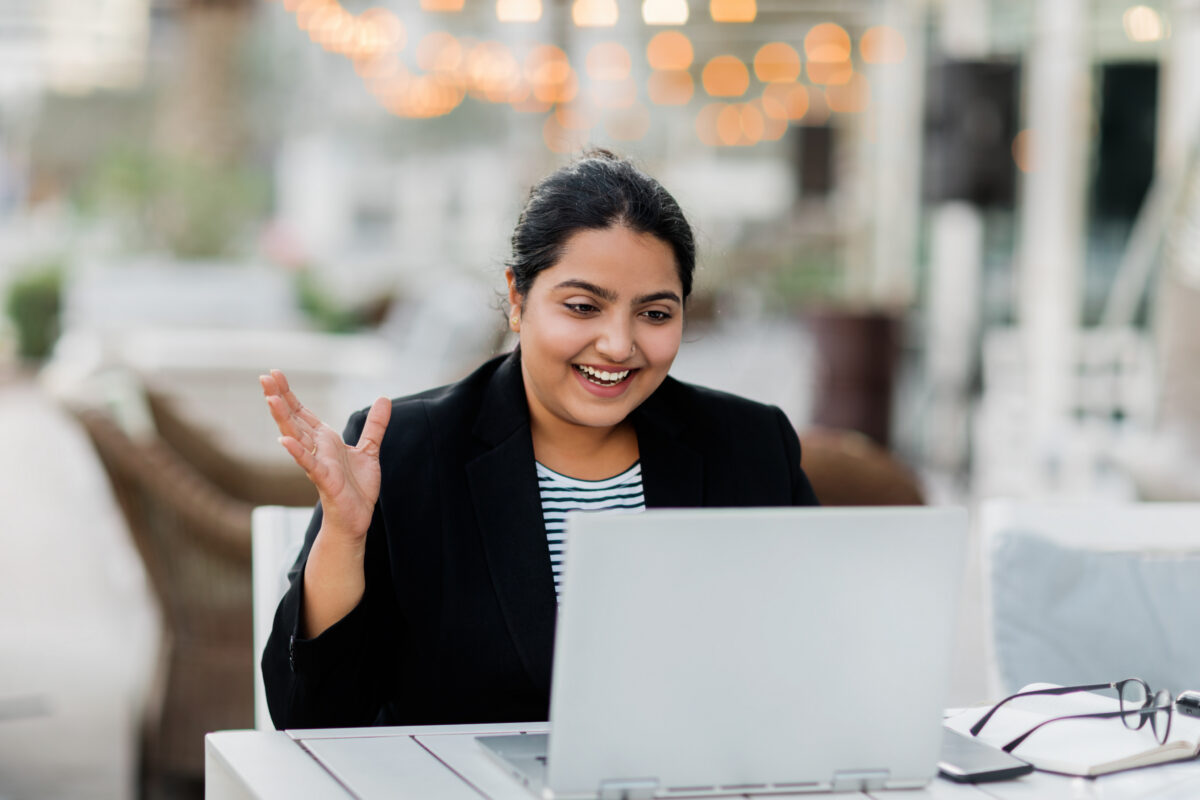 Smiling Woman Black Blazer Gestures While Looking Laptop A smiling woman in a black blazer gestures while looking at a laptop on a table.