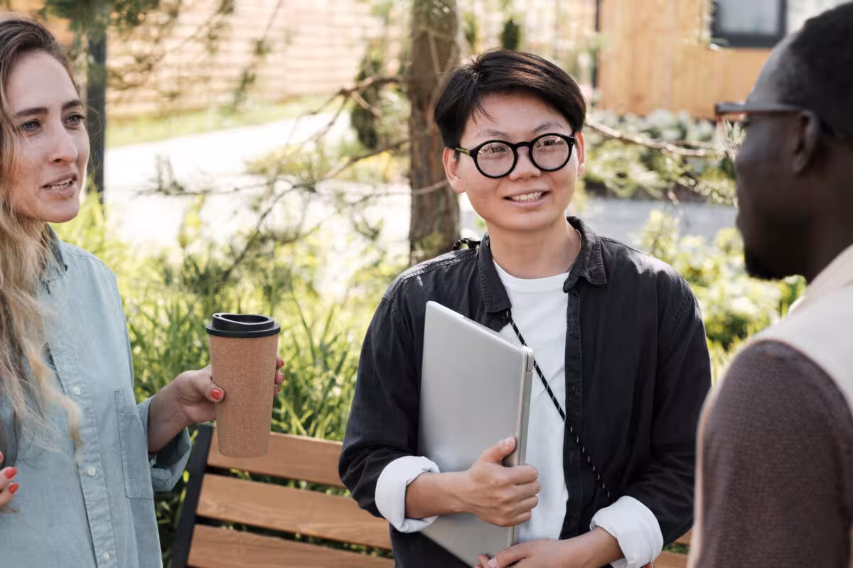Three People Talking Outdoors One Holding Laptop Coffee Three people talking outdoors, one holding a laptop and a coffee cup.