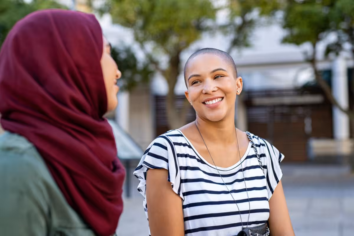 Two Women One Wearing Hijab Other Shaved Head Two women, one wearing a hijab and the other with a shaved head, are talking outside.
