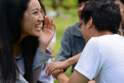 A young Asian woman laughs while her friends play an outdoor game.